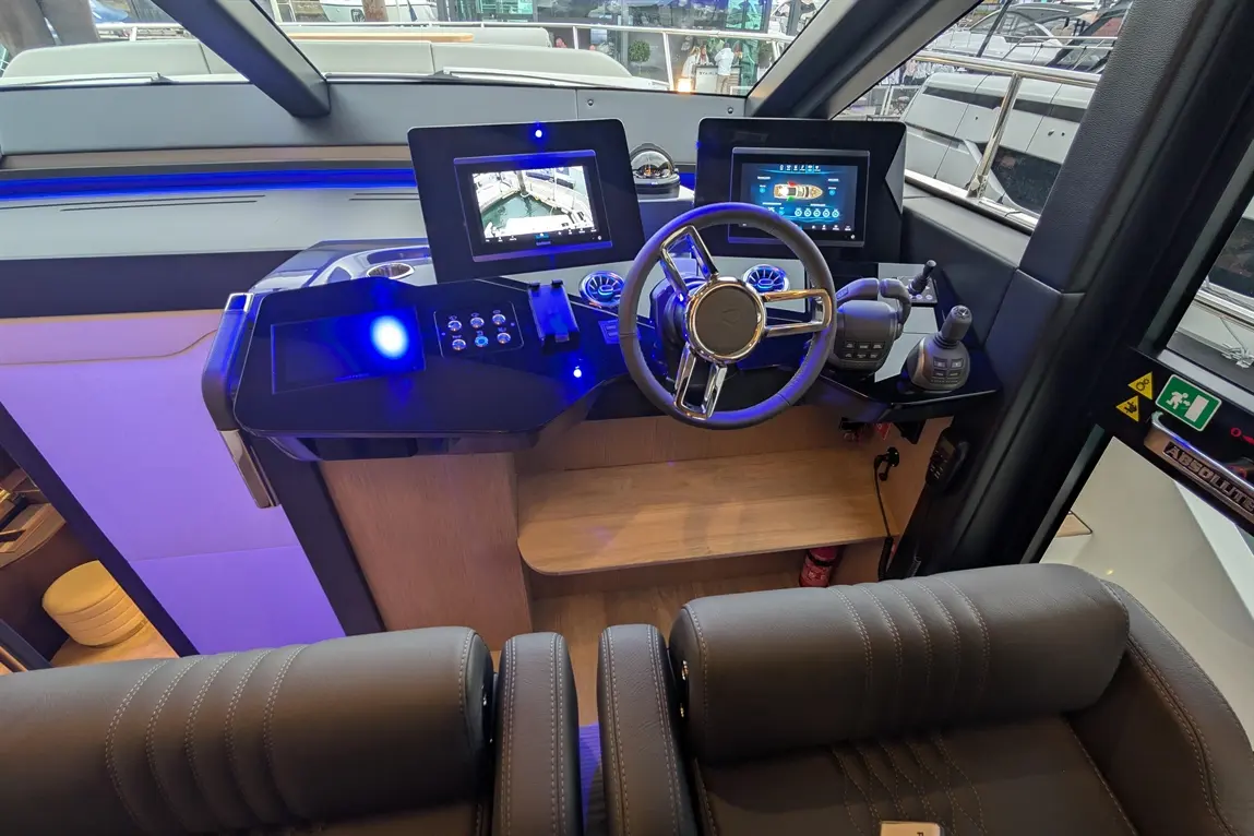 Modern boat dashboard featuring digital displays, steering wheel, control buttons, and luxurious seating.